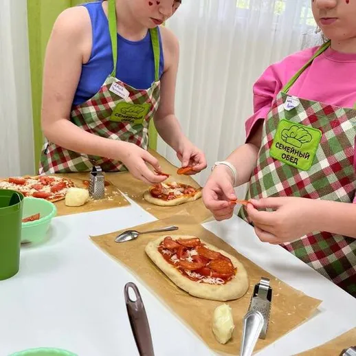 Две девочки готовят пиццу в кулинарном классе, расположенном в уютном помещении с зеленым декором