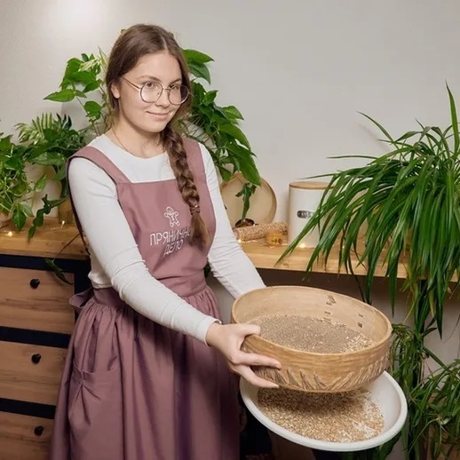 Молодая женщина с ситом для просеивания муки на кухне с зелеными растениями и деревянной мебелью