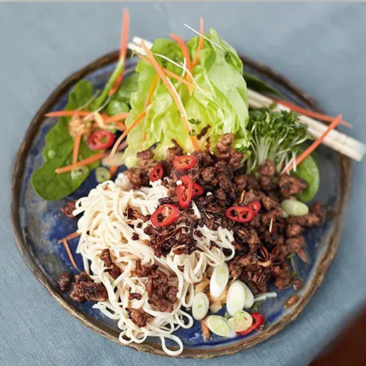 Приятный обед с лапшой, мясом и свежими овощами на синей тарелке