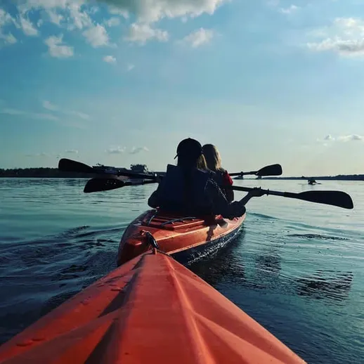 Два человека на каяке плывут по спокойной воде озера под голубым небом в летний день