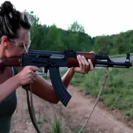 Женщина стреляет из автомата на открытом воздухе в лесистой местности во время заката