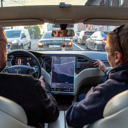 Салон электромобиля Tesla в вечернее время, водитель и пассажир следят за навигацией и движением на дороге