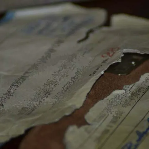 Разорванные старинные документы с рукописными записями на столе, освещенные мягким светом в помещениях музея