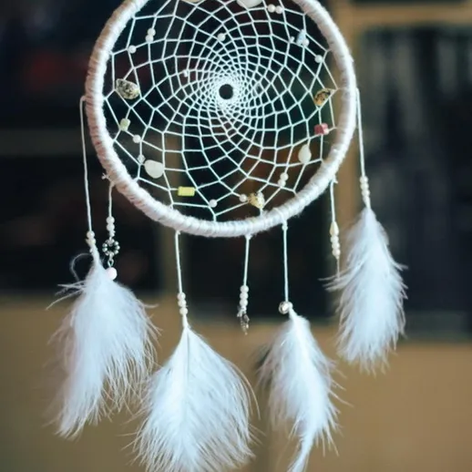 Ловец снов с перьями и бусинами в интерьере уютной комнаты, акцент на деталь рукоделия и текстуры