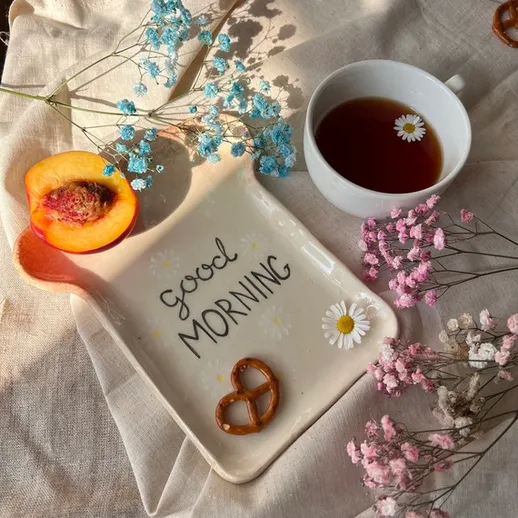 Утренний столик с чашкой чая, тарелкой с закусками и свежими цветами в солнечное утро