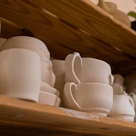 На полке с глиняной посудой, которая готовится к обжигу, в мастерской керамики