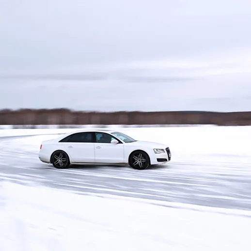 Белый автомобиль скользит по снежной трассе в зимний день на заливной поверхности