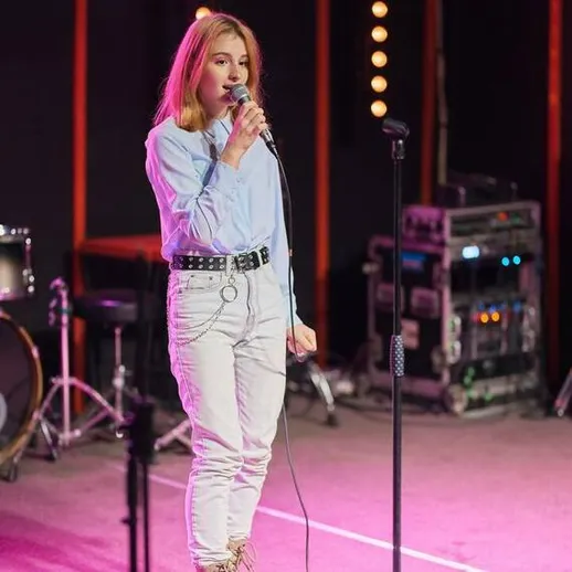 Девушка поет на сцене с микрофоном в культурном центре на концерте в вечернее время