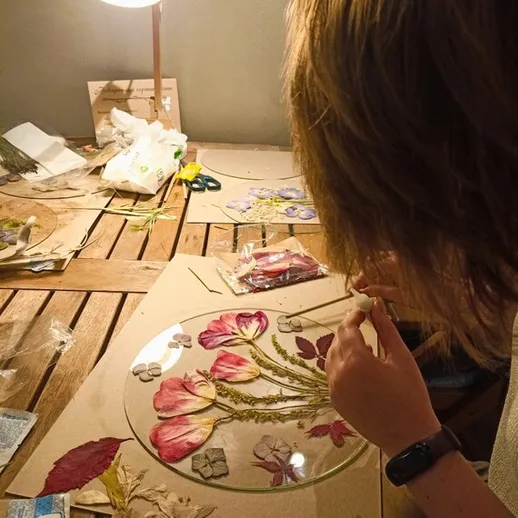 Женщина создает художественное произведение с прессованными цветами на столе в уютной мастерской в вечернее время