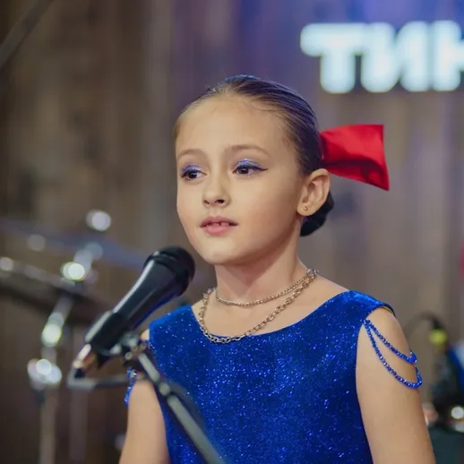 Юная певица выступает на сцене в ярком наряде, демонстрируя свои вокальные способности на музыкальном конкурсе
