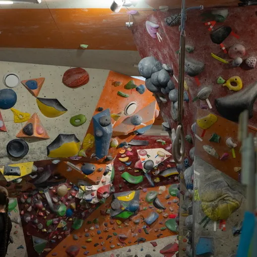 Внутренний скалодром с разноцветными стенками для боулдеринга и спортсменом, занимающимся тренировкой