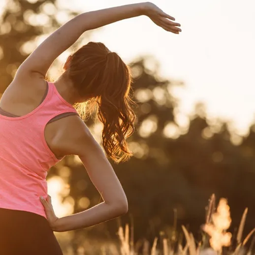 Женщина делает утреннюю растяжку на фоне восхода солнца в поле