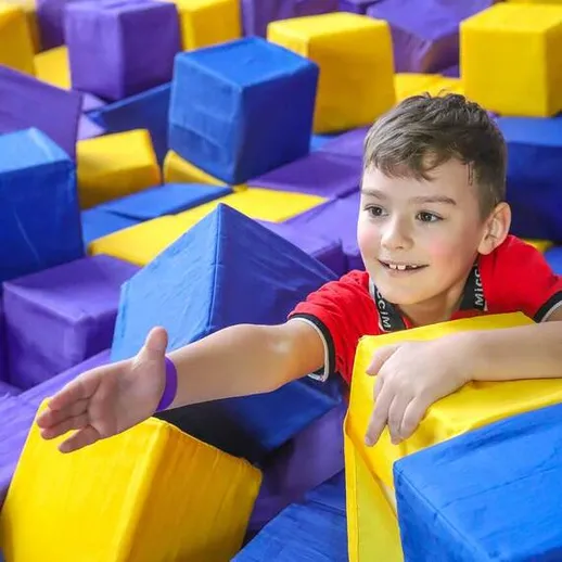 Мальчик играет в аттракционе с мягкими блоками в спортивном центре, наслаждаясь активным отдыхом в летнее время