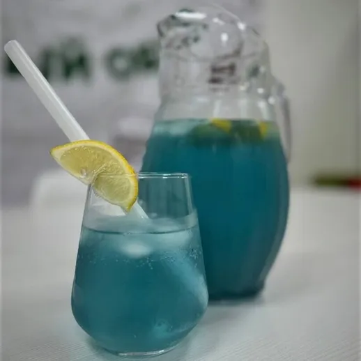 Освежающий голубой напиток с лимоном в стакане и кувшине на столе
