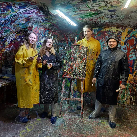 Группа людей в желтых плащах создаёт абстрактное искусство в заброшенной мастерской