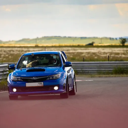 Синий спортивный автомобиль на гоночной трассе под ясным небом в летний день