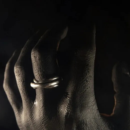 Черная рука с серебряным кольцом на фоне темноты, создающая загадочную атмосферу