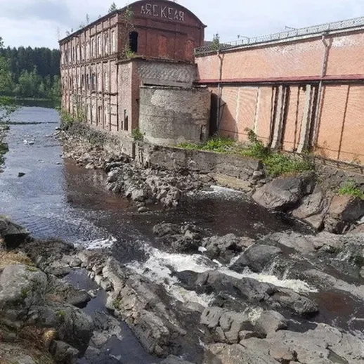 Заброшенное здание у реки с каменистым берегом и порогами в хмурый день осени
