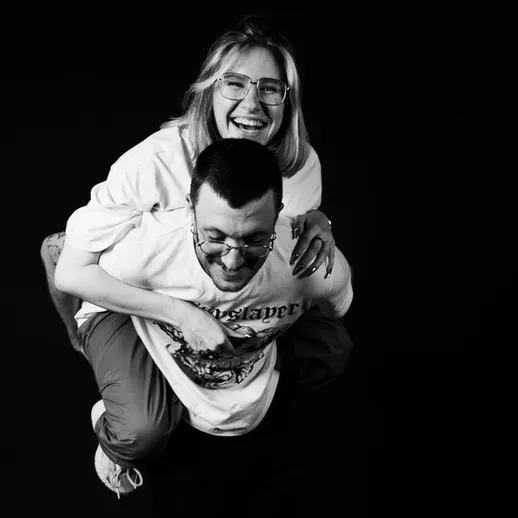 Молодая пара смеется, мужчина поднимает женщину на спине в студии с черным фоном