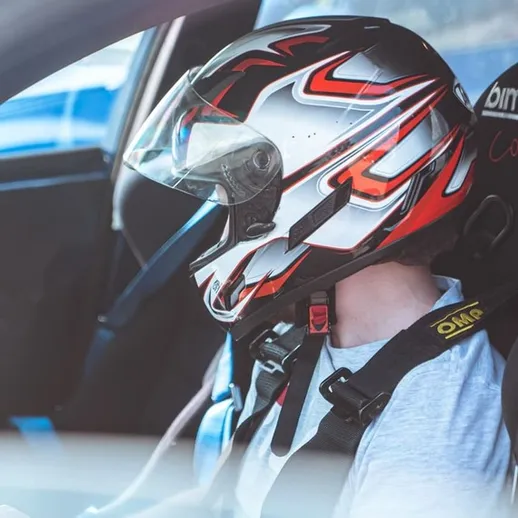 Гоночный пилот в шлеме готовится к заезду на автомобиле на трассе в ясный день