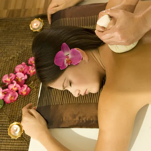 Расслабляющий массаж с травяными мешочками в спа-салоне среди орхидей и свечей в вечернее время