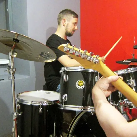 Музыканты играют вместе в репетиционном зале с ударными и гитарой в вечернее время