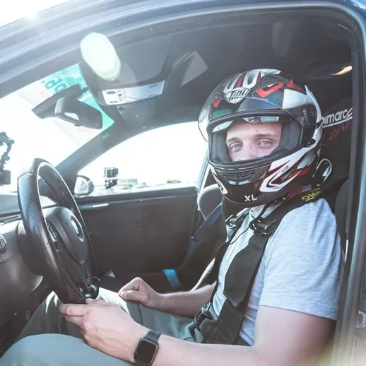 Автомобильный гонщик в шлеме и с ремнями безопасности в спортивной машине на трассе во время соревнований