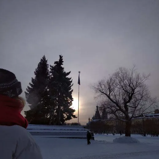 Зимний пейзаж с флагом на фоне заката, снежный парк и люди в теплых одеждах, вечернее время в России