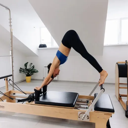 Упражнения на реформере в спортивном зале с высокими потолками и естественным освещением