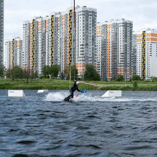 Канатоходец катается на водных лыжах в городской акватории под облачным небом