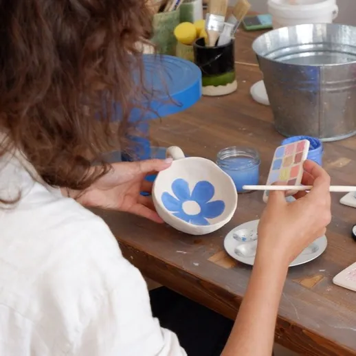 Женщина расписывает кружку в художественной мастерской, используя акриловые краски и палитру для создания узоров