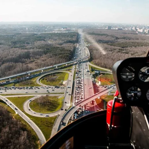 Обзорный полет на вертолете над загруженной автомобильной развязкой в лесной местности недалеко от мегаполиса