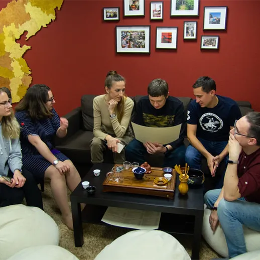 Группа людей обсуждает планы в уютной комнате с красной стеной и картой на фоне