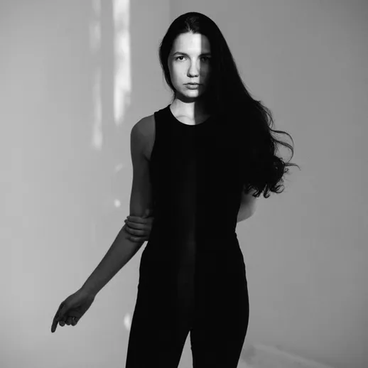 Молодая женщина с длинными волосами в черной одежде позирует в абстрактном пространстве при мягком свете