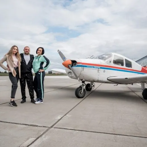 Группа людей позирует возле спортивного самолета на аэродроме в ясный день