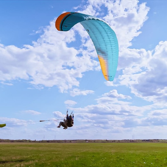 Парапланерист в небе над зеленым полем под голубым небом и облаками в ясный солнечный день