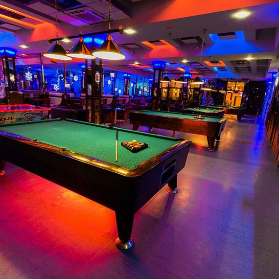 Современный бильярдный зал с яркой подсветкой и множеством игровых столов в вечернее время Современный бильярдный зал с яркой подсветкой и множеством игровых столов в вечернее время