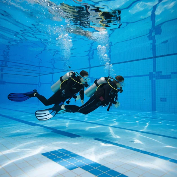 Два человека занимаются дайвингом в бассейне, погружая оборудование под воду. Главное фото