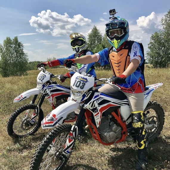 Два мотоциклиста на спортивных мотоциклах готовятся к заезду на травяной местности в солнечный день