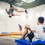 Тренировка акробатов на батутах в спортзале, люди выполняют трюки и жонглируют в тренажерном зале - превью 1