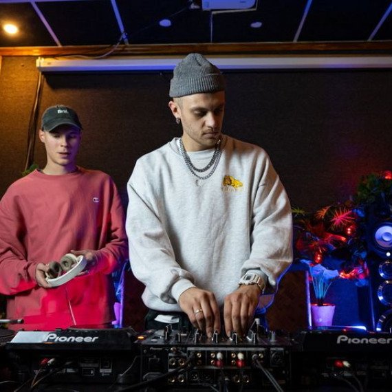 Музыканты работают на диджейском оборудовании в студии с ярким декором. Главное фото