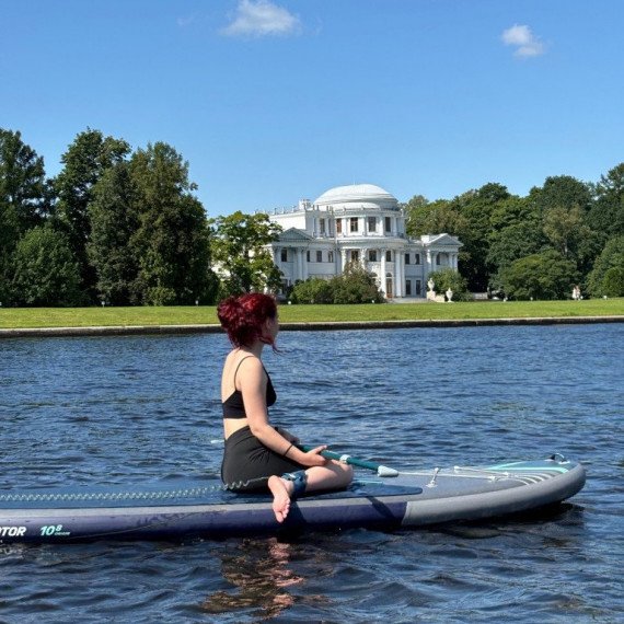 Женщина на вечернем паддлборде на озере рядом с историческим зданием в солнечный день Женщина на вечернем паддлборде на озере рядом с историческим зданием в солнечный день