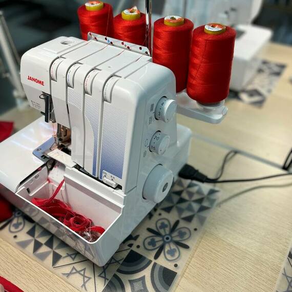 Швейная машинка Janome на столе с яркой красной ниткой в мастерской по пошиву одежды. Фото 9