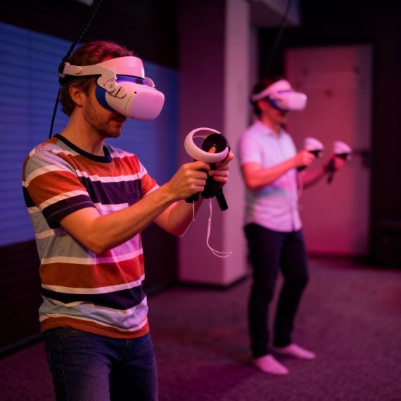 Два человека играют в виртуальной реальности в комнате с низким светом и технологическим оборудованием Два человека играют в виртуальной реальности в комнате с низким светом и технологическим оборудованием