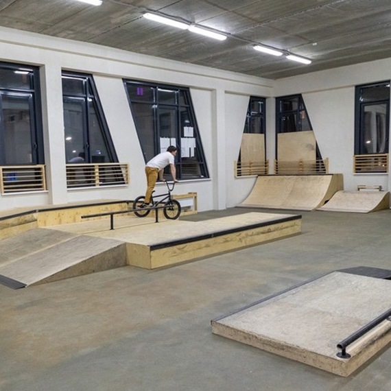 Скейтпарк в помещении с райдером на BMX в процессе выполнения трюка в вечернее время. Фото 9