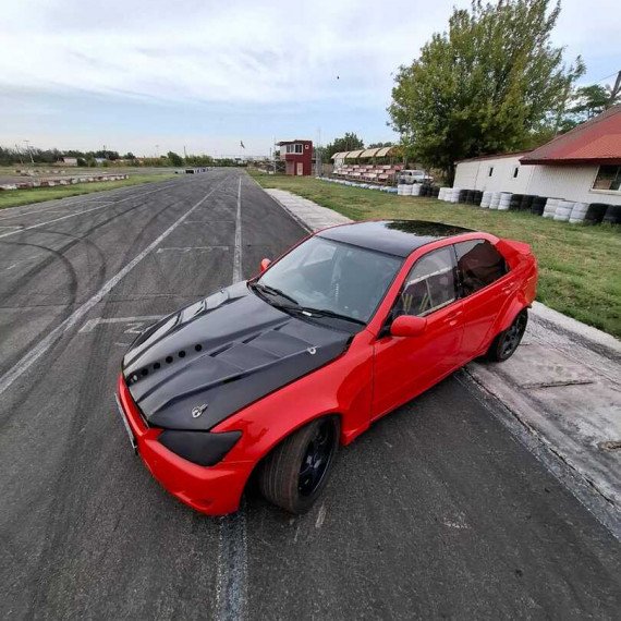 Красный спортивный автомобиль на треке для дрифта в автодроме на фоне зелёных деревьев