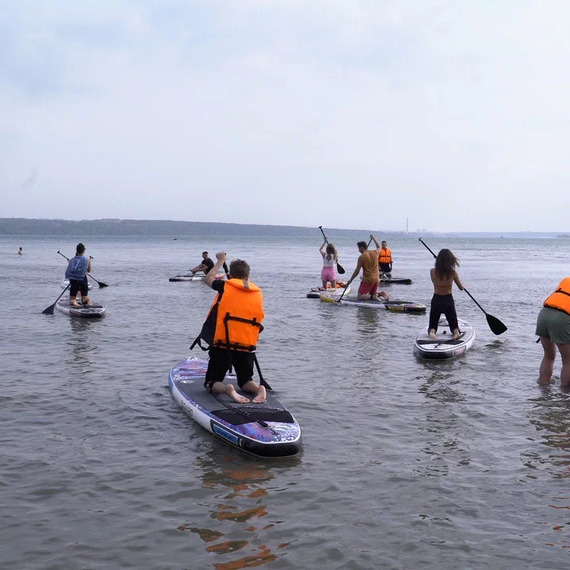 Групповая тренировка по паддлбордингу на спокойной воде у берега в ярких жилетах спасателей. Фото 13