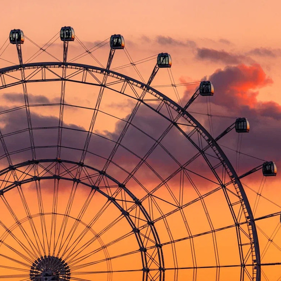 Огромное колесо обозрения на фоне заката в городе, завораживающее зрителей яркими огнями