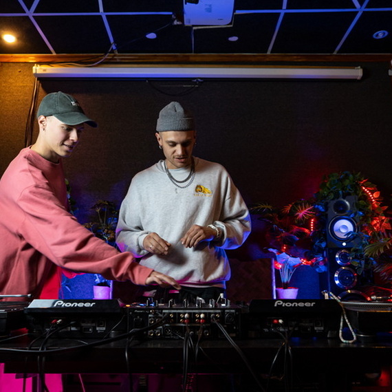 Два диджея работают за пультами в студии звукозаписи с эффектным освещением Два диджея работают за пультами в студии звукозаписи с эффектным освещением