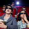 Молодые люди смотрят фильм в 3D в кинотеатре с попкорном в руках, яркий экран освещает зал - превью 1